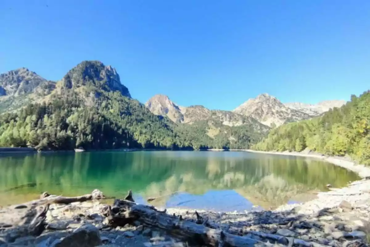 Un llac envoltat de muntanyes i boscos sota un cel clar. Un llac envoltat de muntanyes i boscos sota un cel clar.