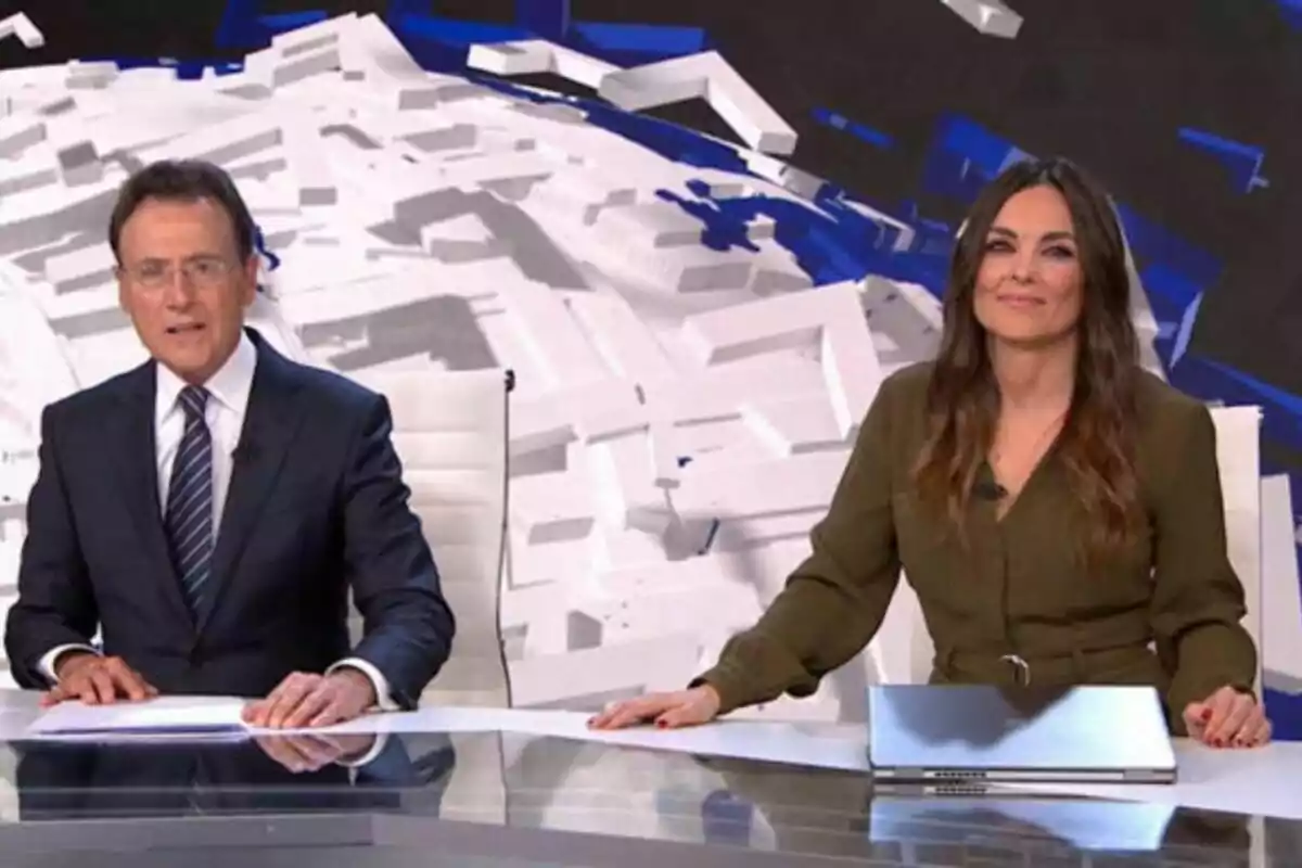 Matías Prats i Mónica Carrillo a Antena 3 Notícies asseguts en un estudi de televisió amb un fons geomètric. Matías Prats i Mónica Carrillo a Antena 3 Notícies asseguts en un estudi de televisió amb un fons geomètric.