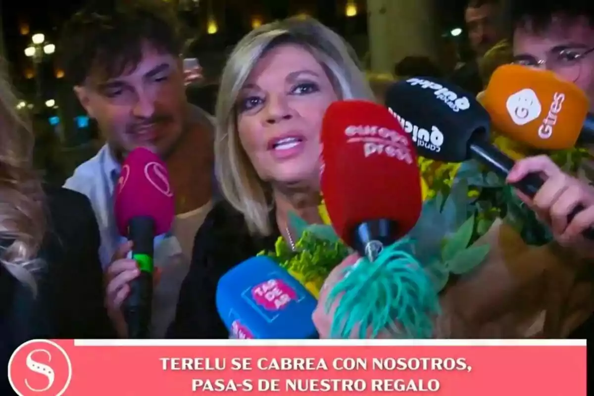 Terelu Campos envoltada de micròfons de diferents mitjans de comunicació mentre sosté un ram de flors a Socialité. Terelu Campos envoltada de micròfons de diferents mitjans de comunicació mentre sosté un ram de flors a Socialité.
